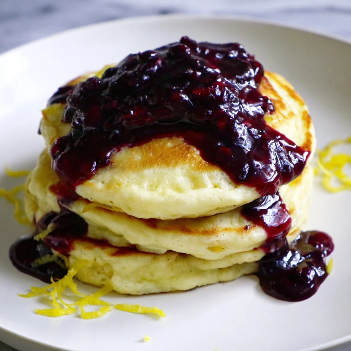 Golden brown Lemon Ricotta Pancakes drizzled with vibrant blueberry syrup, ready to savor.