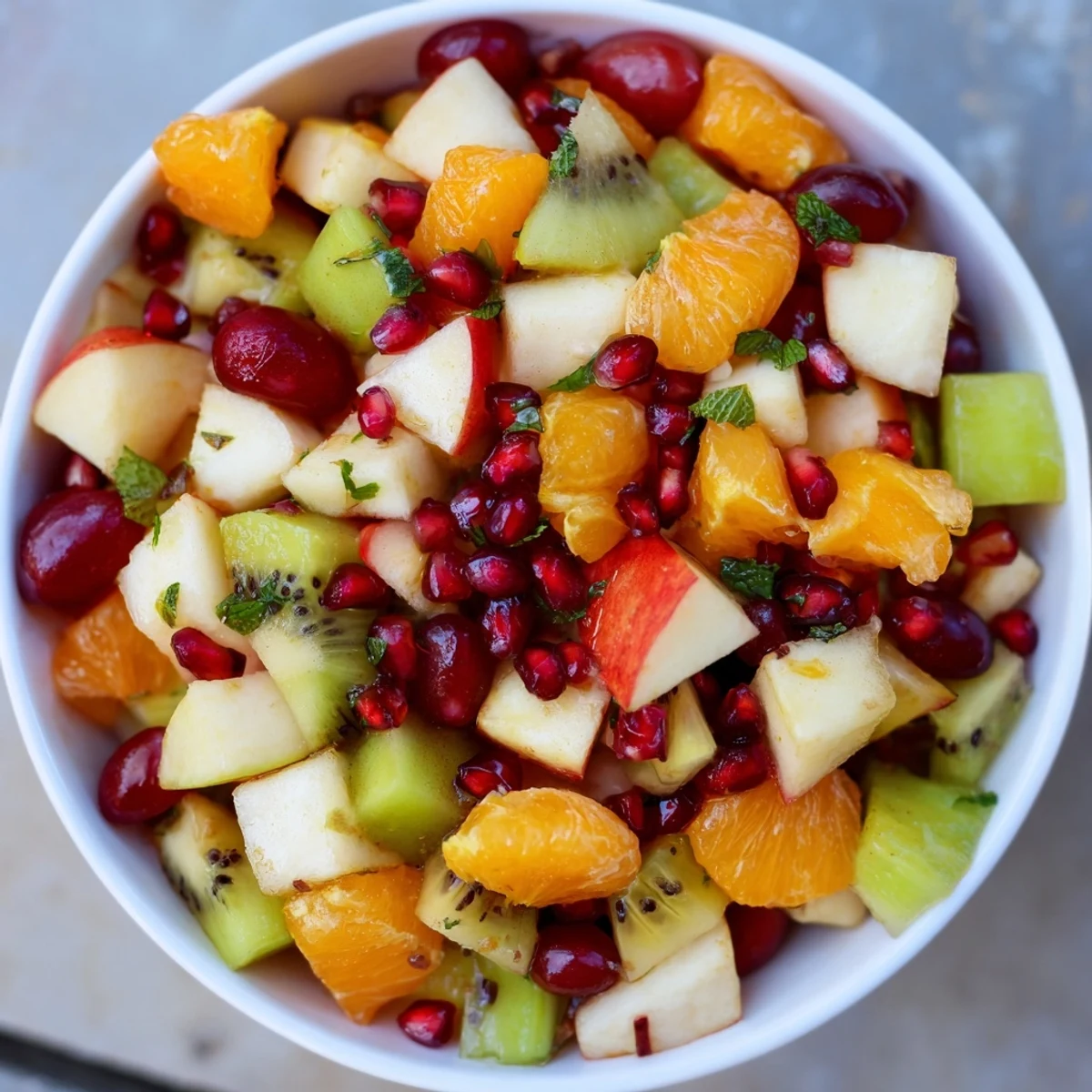Winter Fruit Salad with Mint and Honey served in a glass bowl, featuring bright citrus segments, diced apples, and pomegranate arils drizzled with honey.