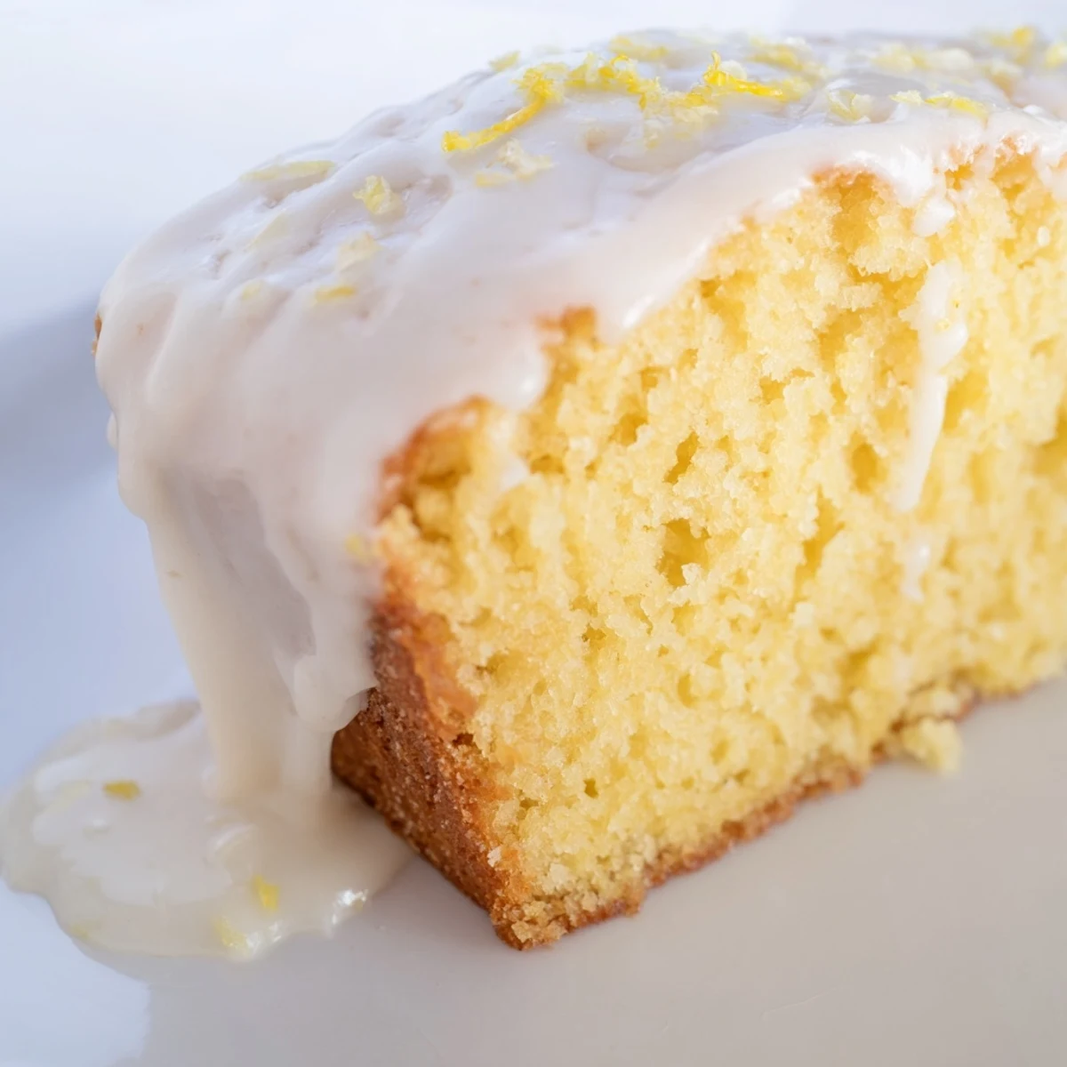 Golden, moist Lemon Loaf Cake with Icing drizzled over the top, displayed on a rustic wooden serving board.