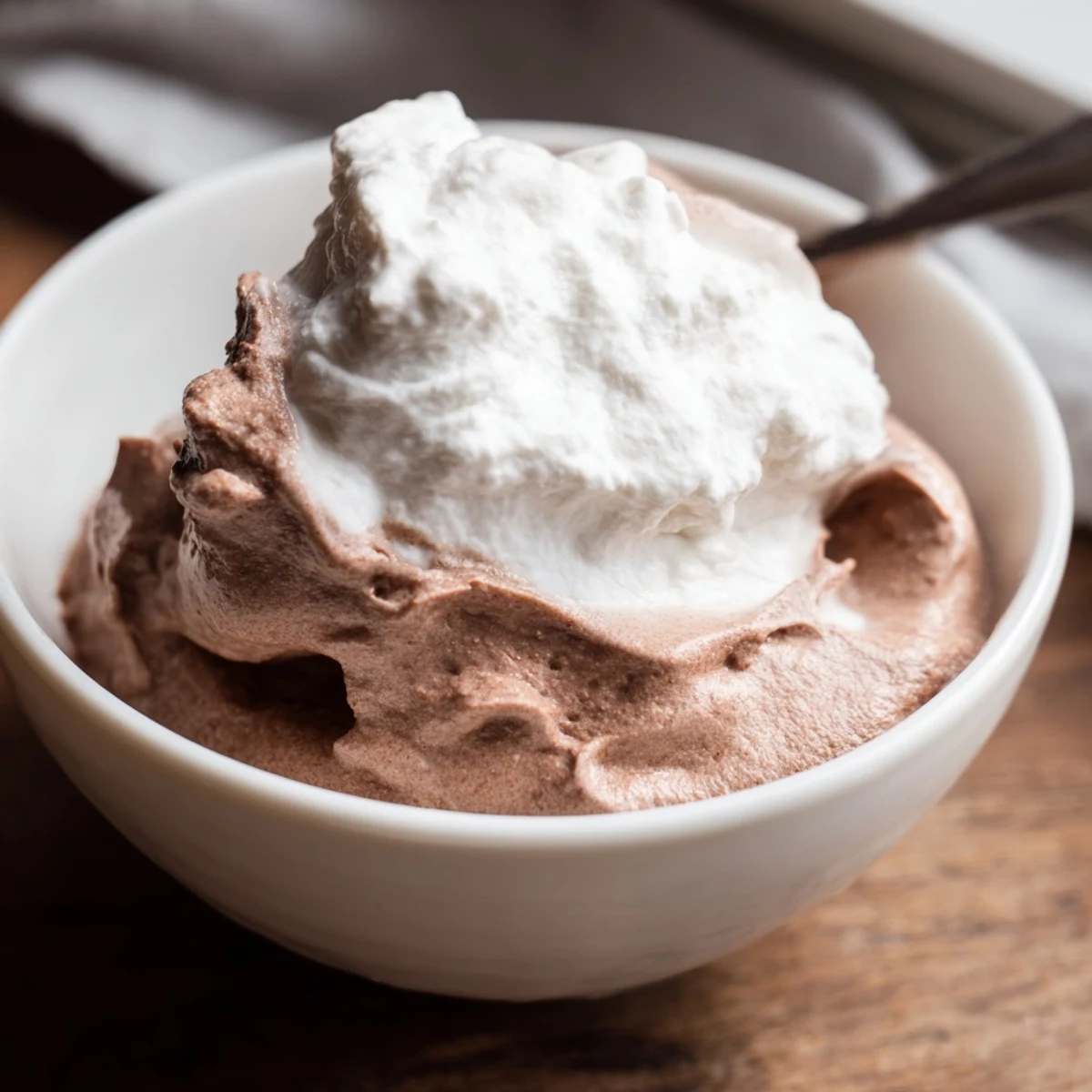 Warm, freshly made chocolate pudding with whipped cream melting slightly, ready to enjoy as a comforting sweet treat.