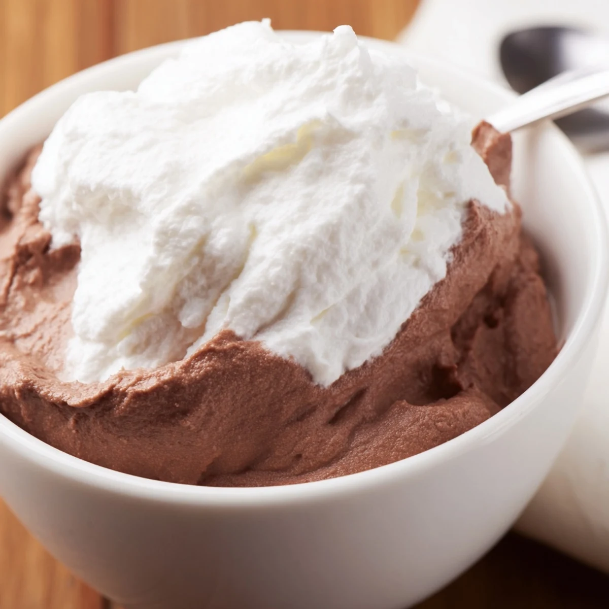 Homemade chocolate pudding garnished with whipped cream and chocolate shavings, perfect for serving at dinner parties or family gatherings.