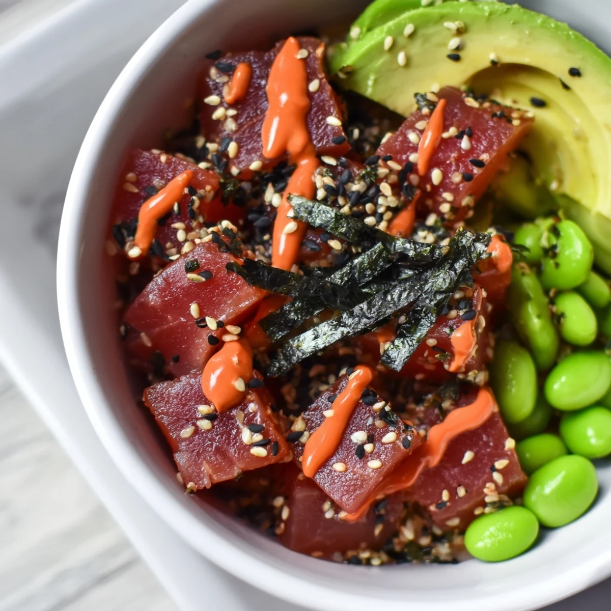A close-up of a Spicy Tuna Poke Bowl topped with creamy avocado and a drizzle of spicy sriracha mayo.