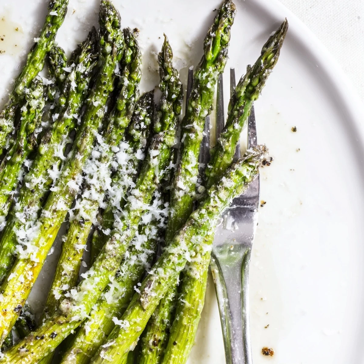 Roasted Asparagus with Parmesan Cheese is served hot, garnished with fresh parsley and lemon wedges on a plate.
