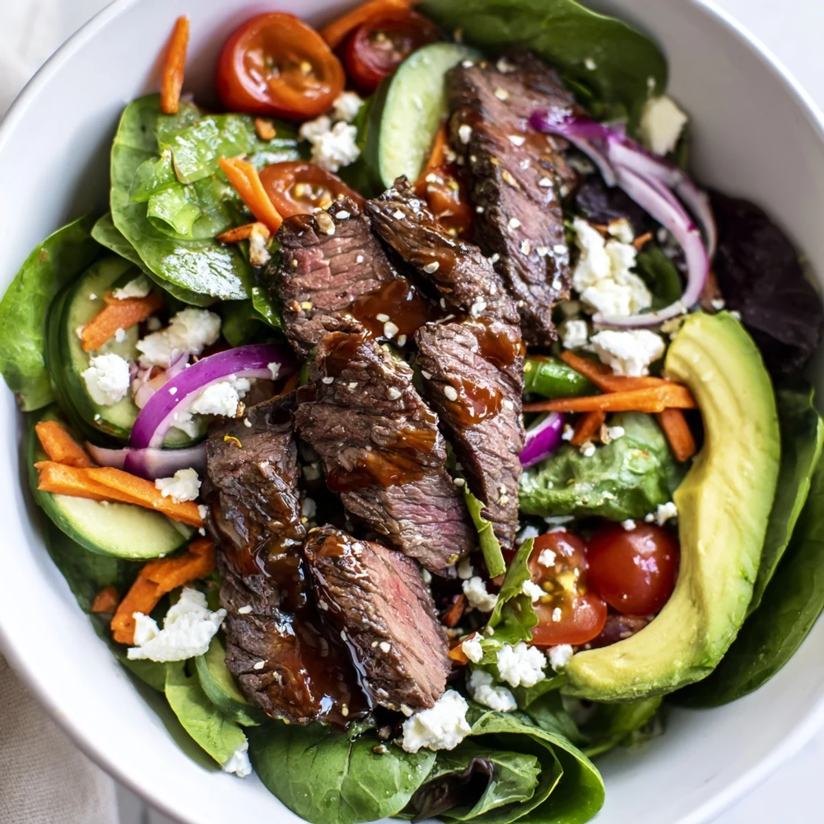 Sliced seared beef rests atop a bed of mixed greens, cucumbers, and cherry tomatoes in a Beef Salad Bowl.