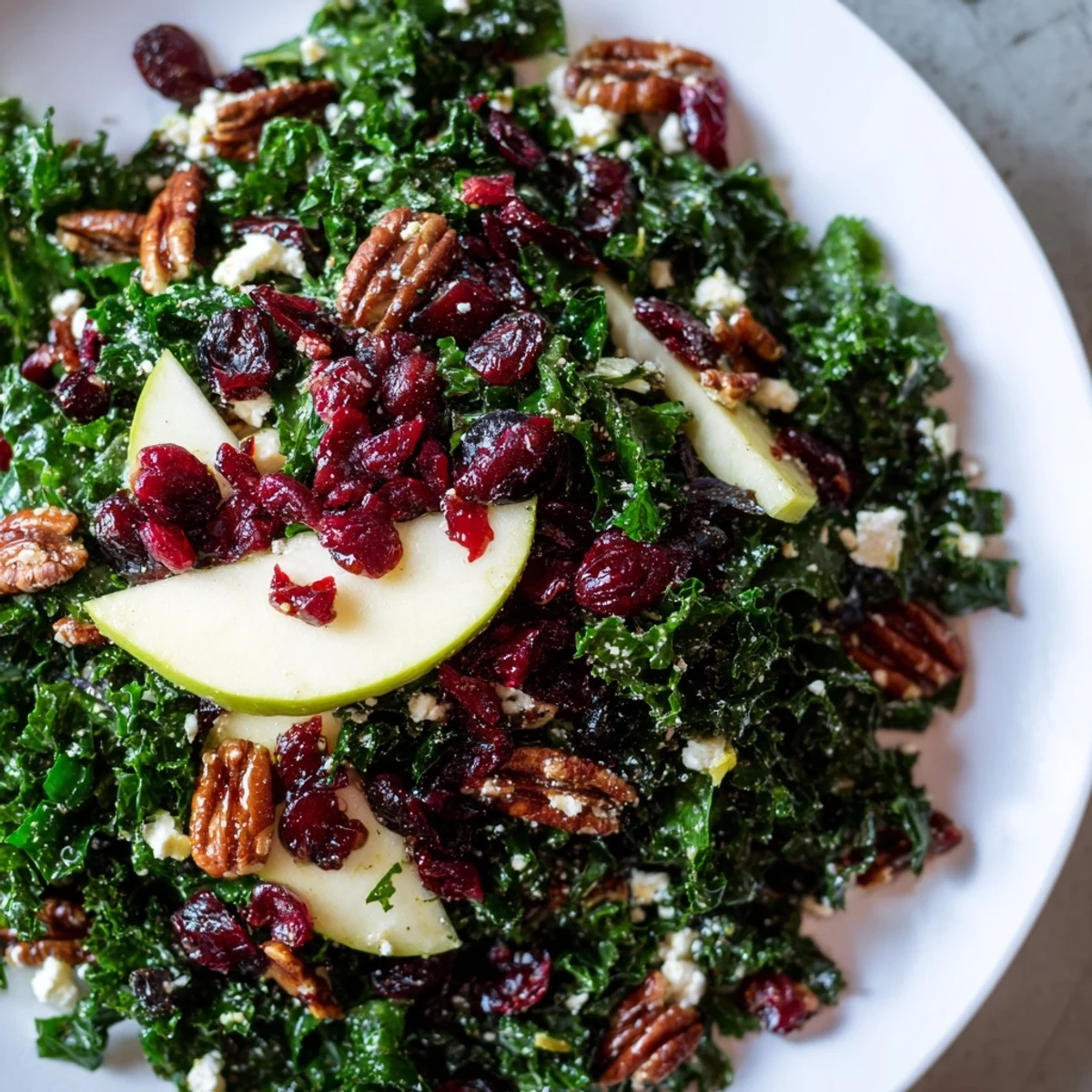 Freshly tossed Winter Kale Salad with Dried Cranberries, featuring vibrant kale leaves and sliced apples on a white ceramic plate.
