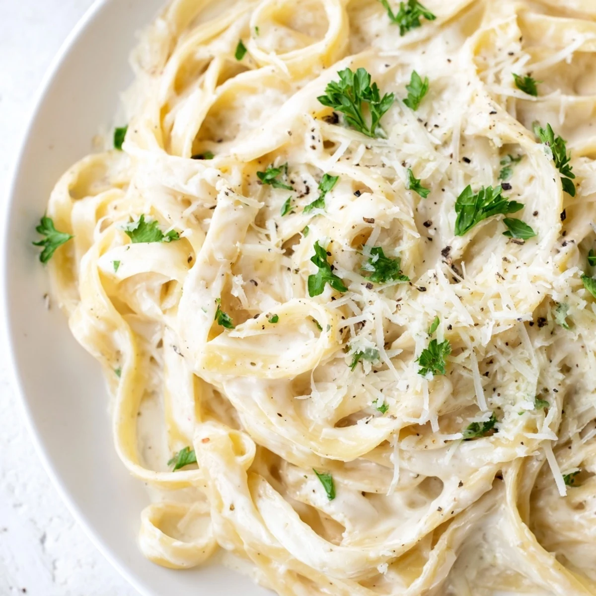 Golden fettuccine pasta coated in creamy Alfredo sauce with a garnish of fresh parsley and grated Parmesan cheese.