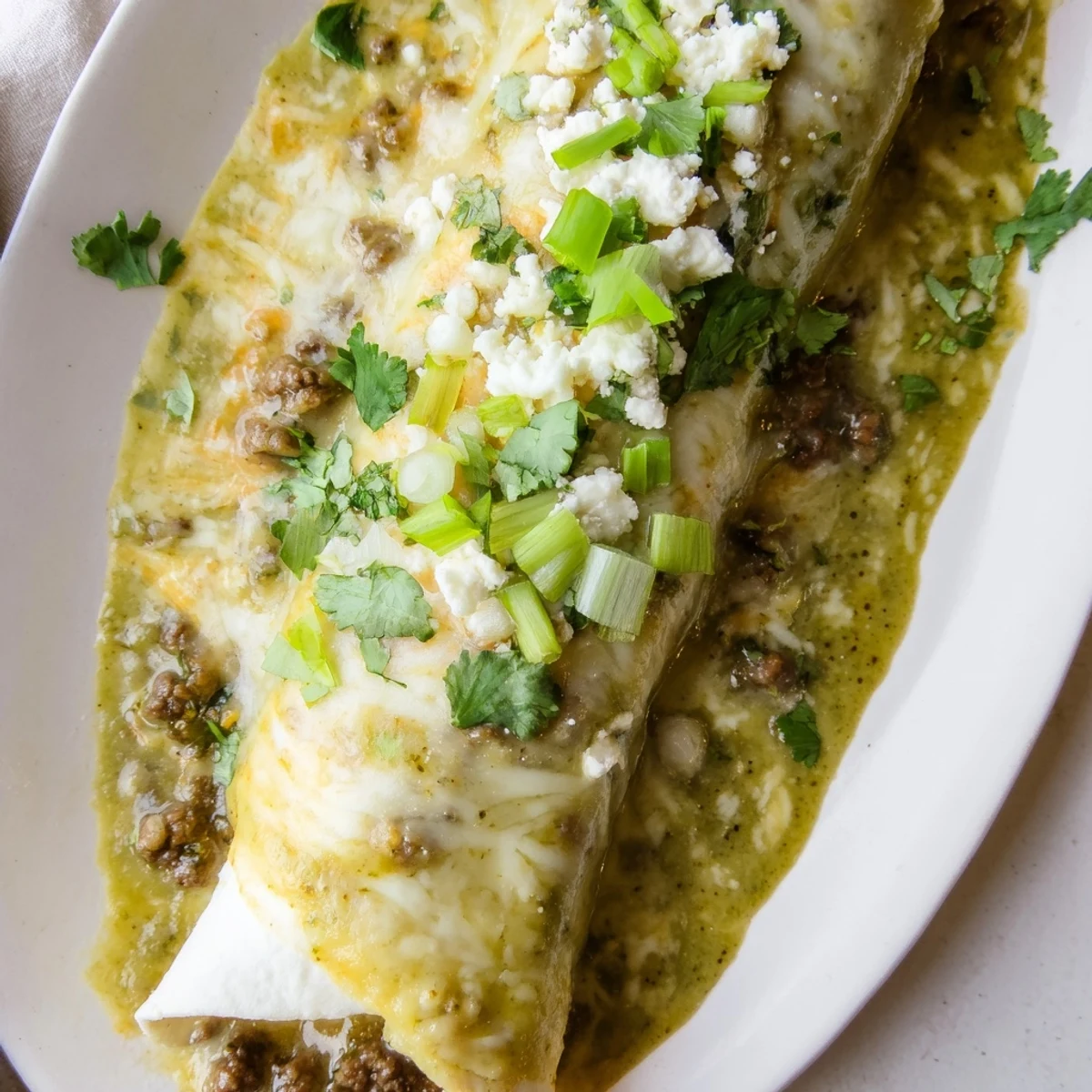 A skillet of savory ground beef filling and creamy green enchilada sauce, ready for assembling.