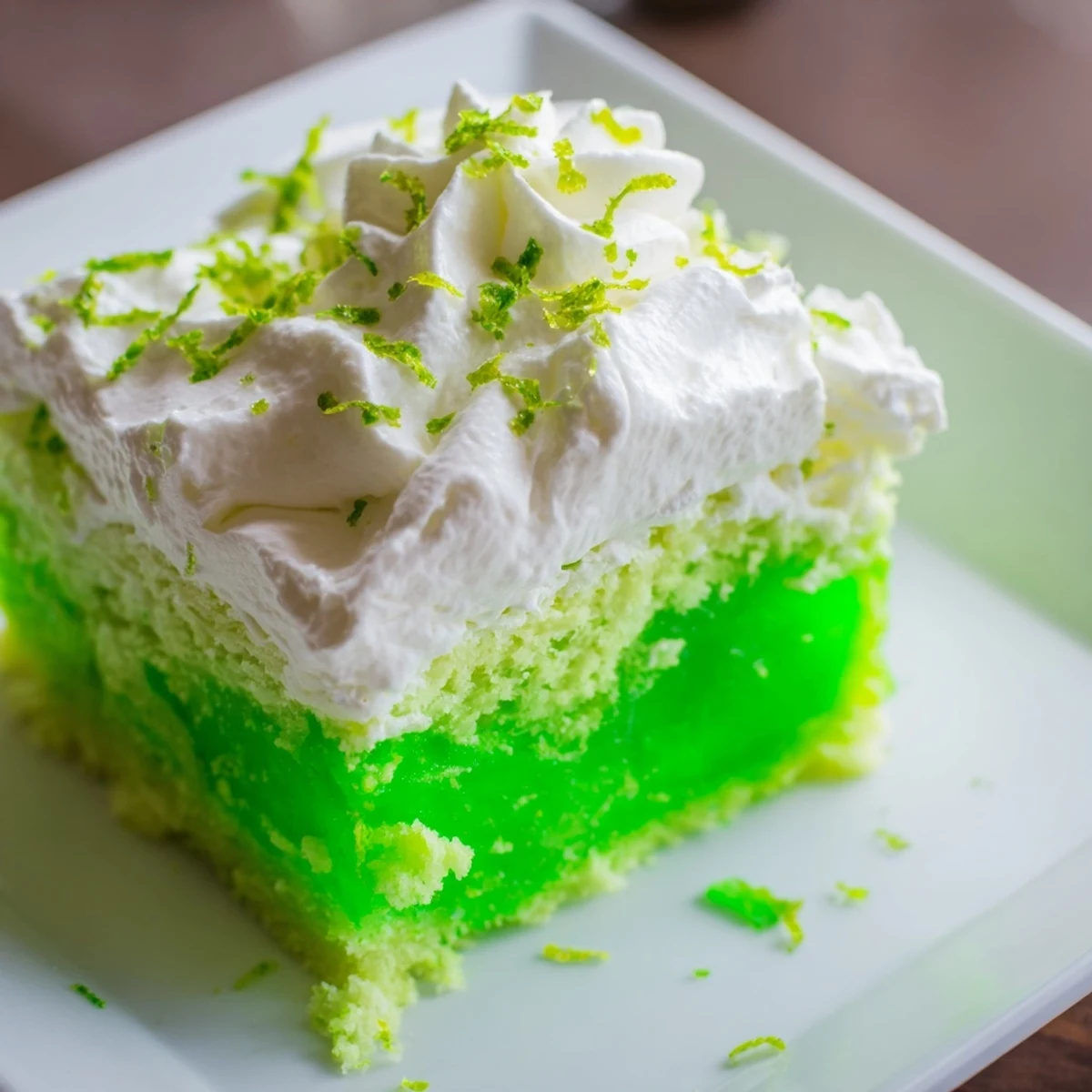A festive St. Patricks Day Lime Poke Cake on a dessert table, topped with a swirl of whipped cream and bright lime zest garnish.
