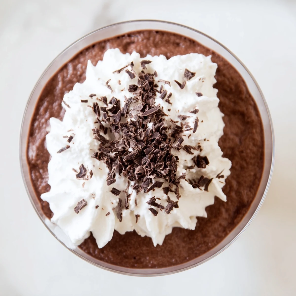 Close-up of Chocolate Mousse with Whipped Cream Shavings topped with delicate chocolate curls on a marble counter.