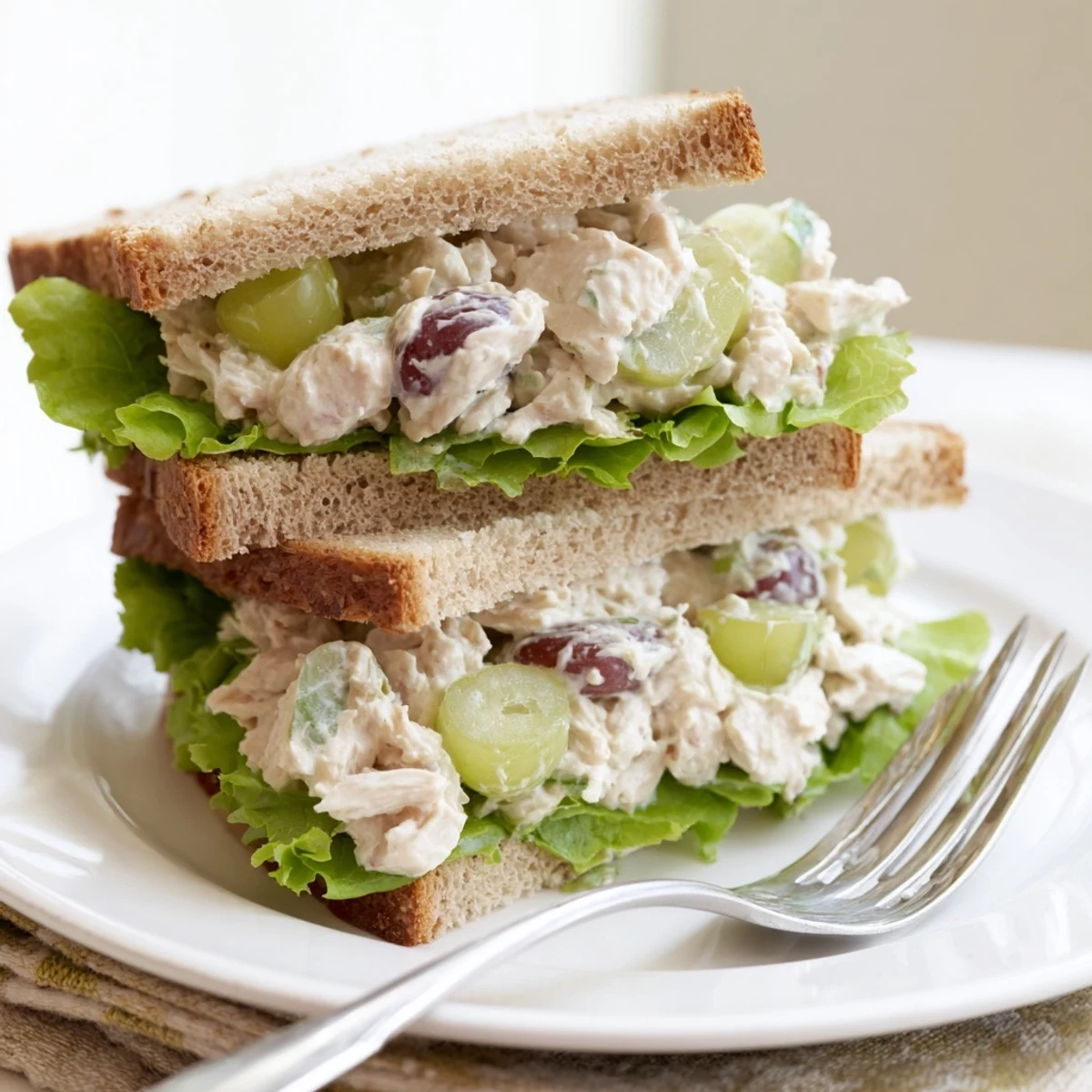 A close-up of a grilled chicken salad sandwich with halved grapes and fresh herbs, served on artisan sourdough.  