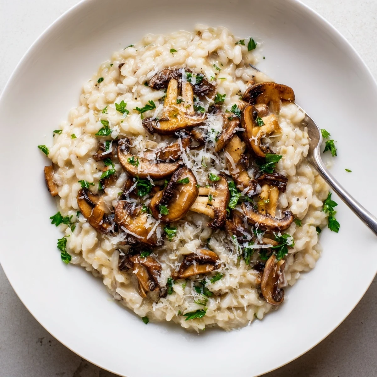 A spoon dips into Creamy Mushroom Risotto with Parmesan, revealing a rich, velvety texture and sautéed cremini mushrooms.