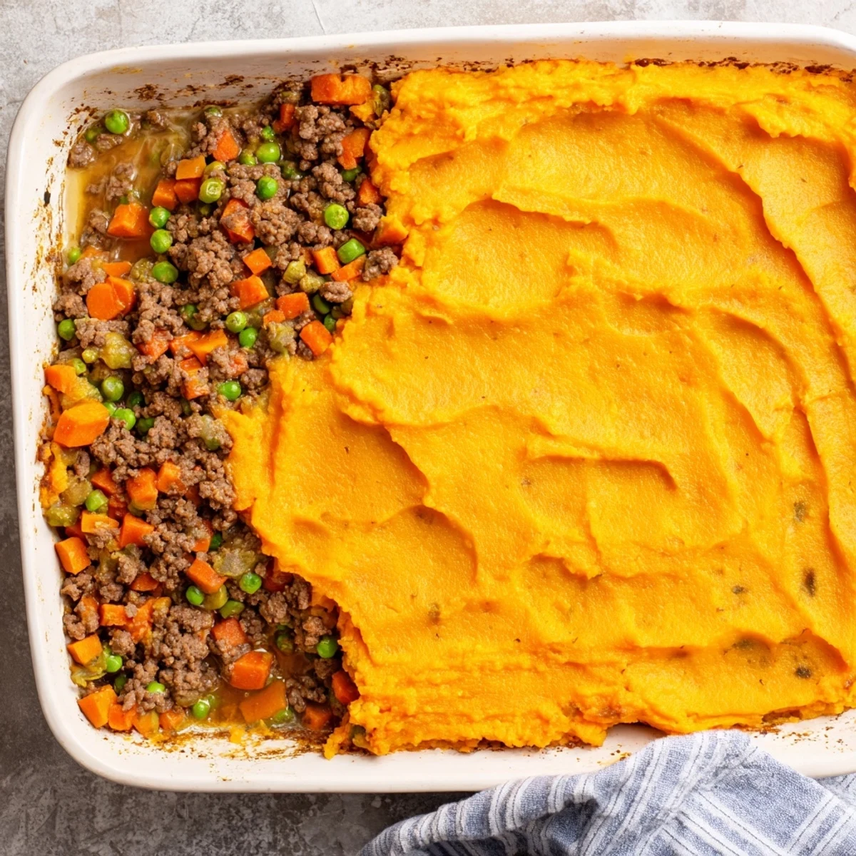 A rustic casserole dish holds freshly baked Beef Shepherds Pie with Sweet Potato, featuring a creamy, golden-orange topping and a savory beef filling.