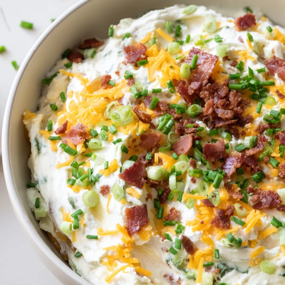 Creamy loaded baked potato dip topped with scallions and bacon bits alongside a pile of golden potato chips, perfect for an easy gluten-free party appetizer.