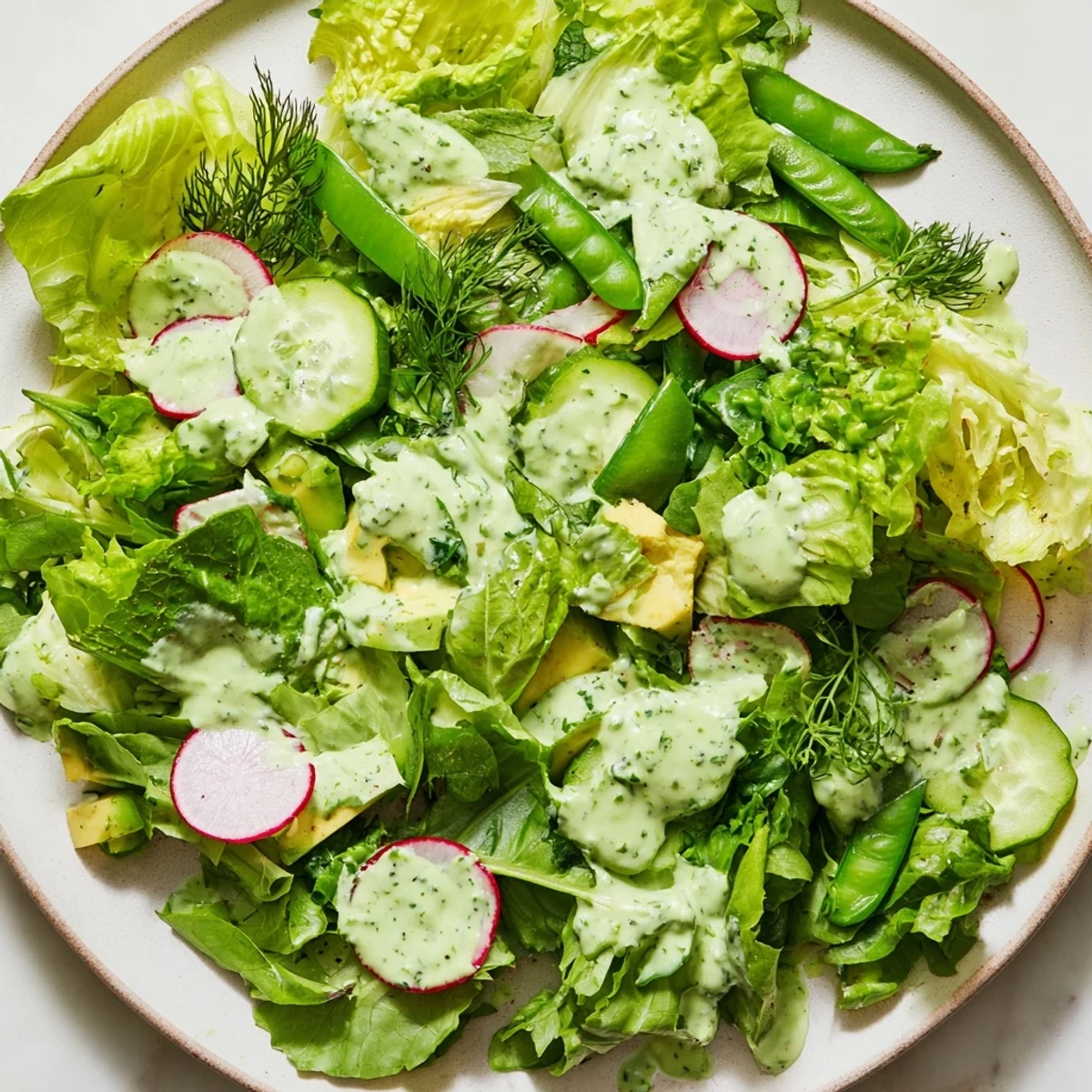 A vibrant Green Salad with Green Goddess Dressing, featuring crisp greens, cucumbers, and creamy avocado tossed in herbaceous dressing.  