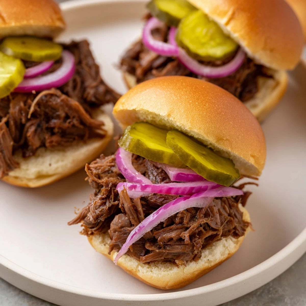 Golden-brown, slow-cooked shredded beef mounded on toasted slider buns with pickles and red onions.