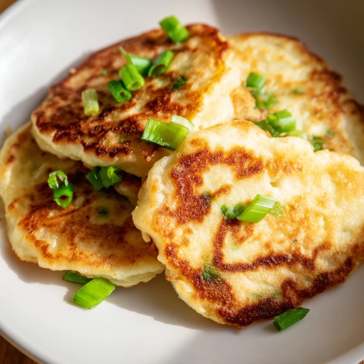 Platter of freshly cooked Irish Boxty Potato Pancakes with Scallions, garnished with extra green onions and served alongside sour cream.  