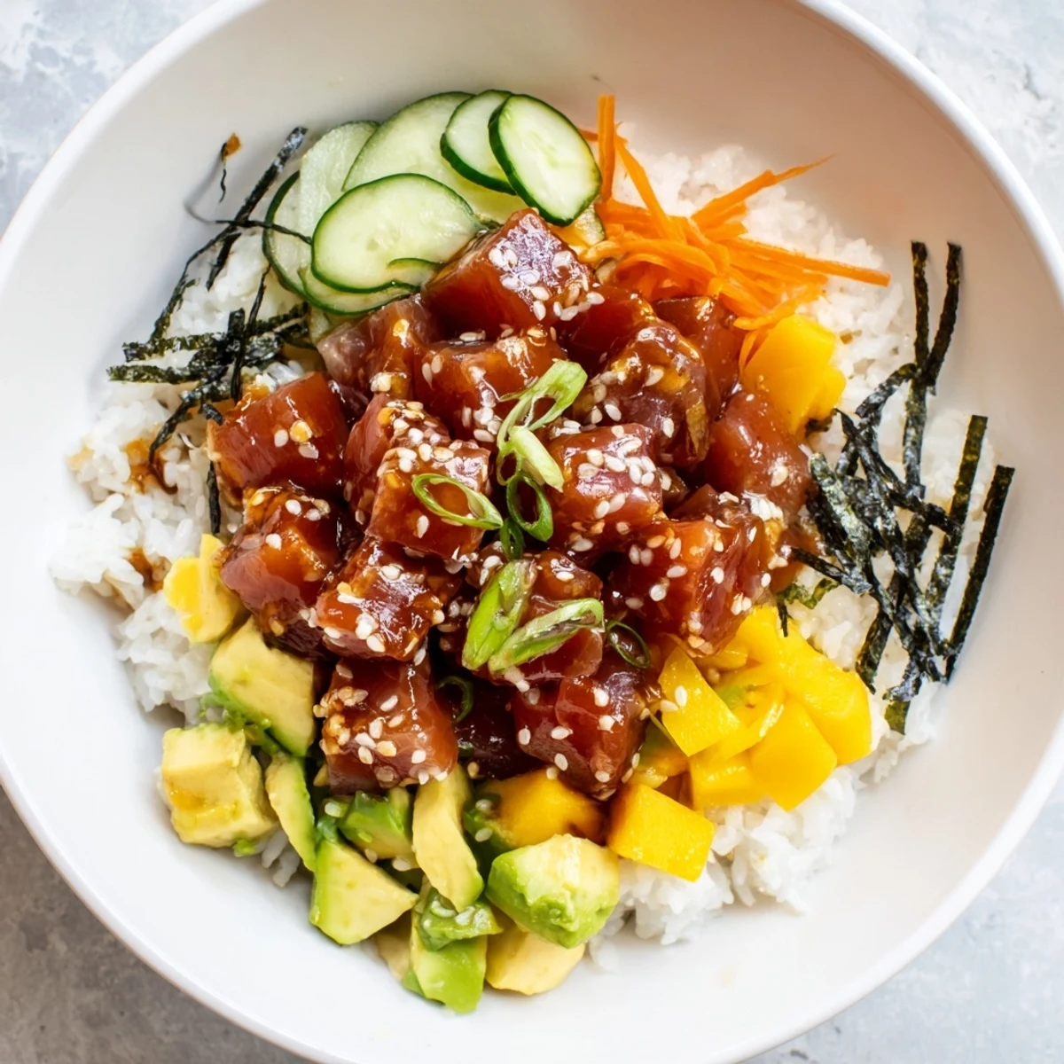 A close-up of Spicy Tuna Poke Bowl with Mango and Avocado garnished with sesame seeds, nori strips, and bright mango chunks.