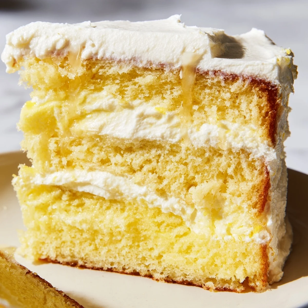 A slice of Limoncello Mascarpone Cake on a white plate reveals light sponge, mascarpone cream, and bright lemon zest garnish.