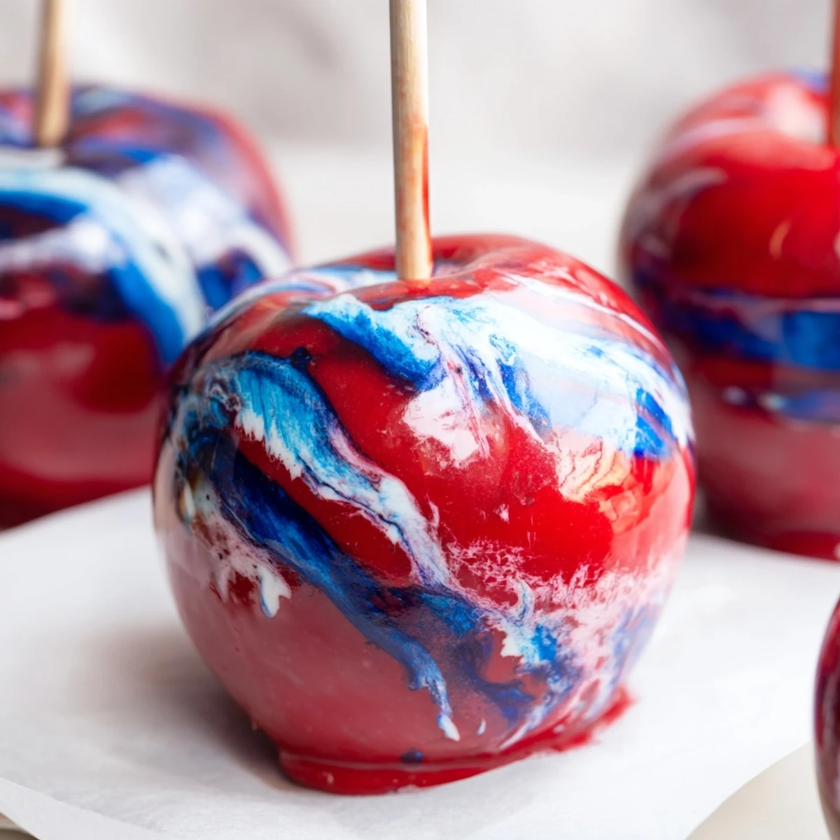 Close-up view of marbled effect candy apples showing glossy texture and swirled candy shell on parchment paper.