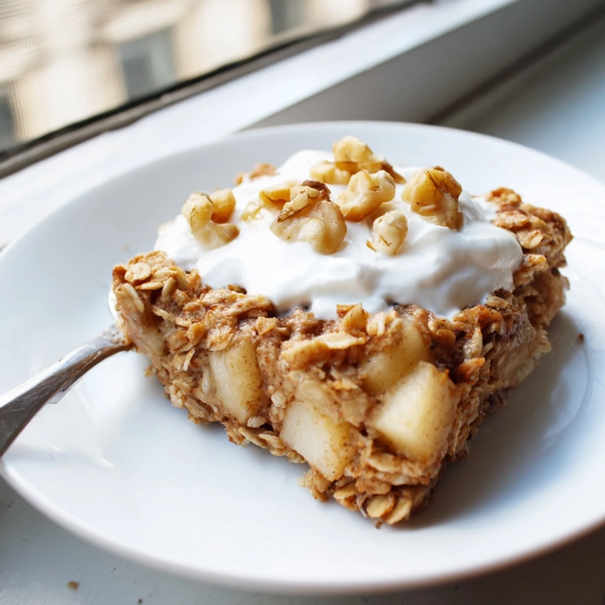 Warm baked apple oatmeal squares topped with creamy Greek yogurt and chopped walnuts on a rustic plate.