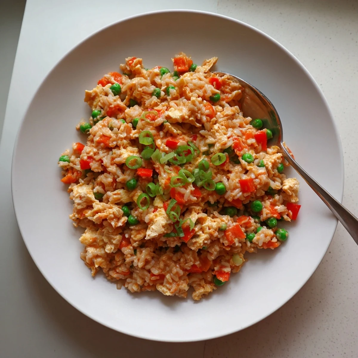 Close-up of Bang Bang Fried Rice with red peppers, peas, and carrots, served steaming hot on a white plate. 