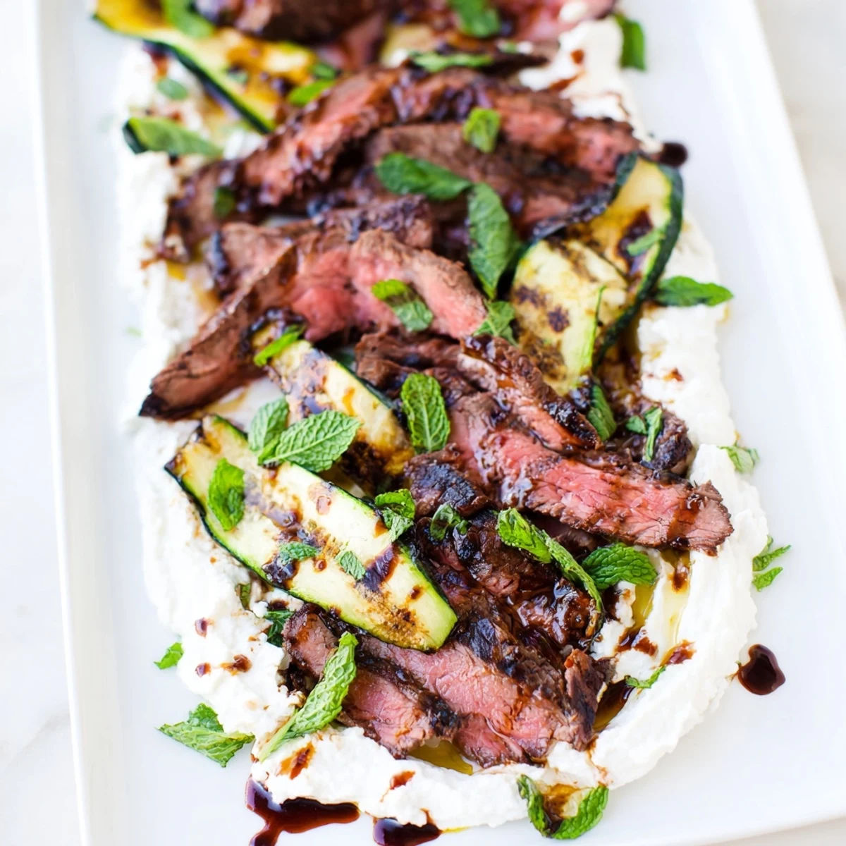 Juicy Balsamic Flank Steak With Grilled Zucchini And Whipped Feta shines with glistening glaze and smoky grill marks on zucchini.
