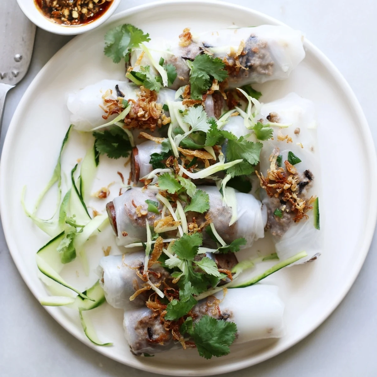 Silky white Banh Cuon rolls filled with savory pork and mushrooms, garnished with fried shallots and cucumber slices.