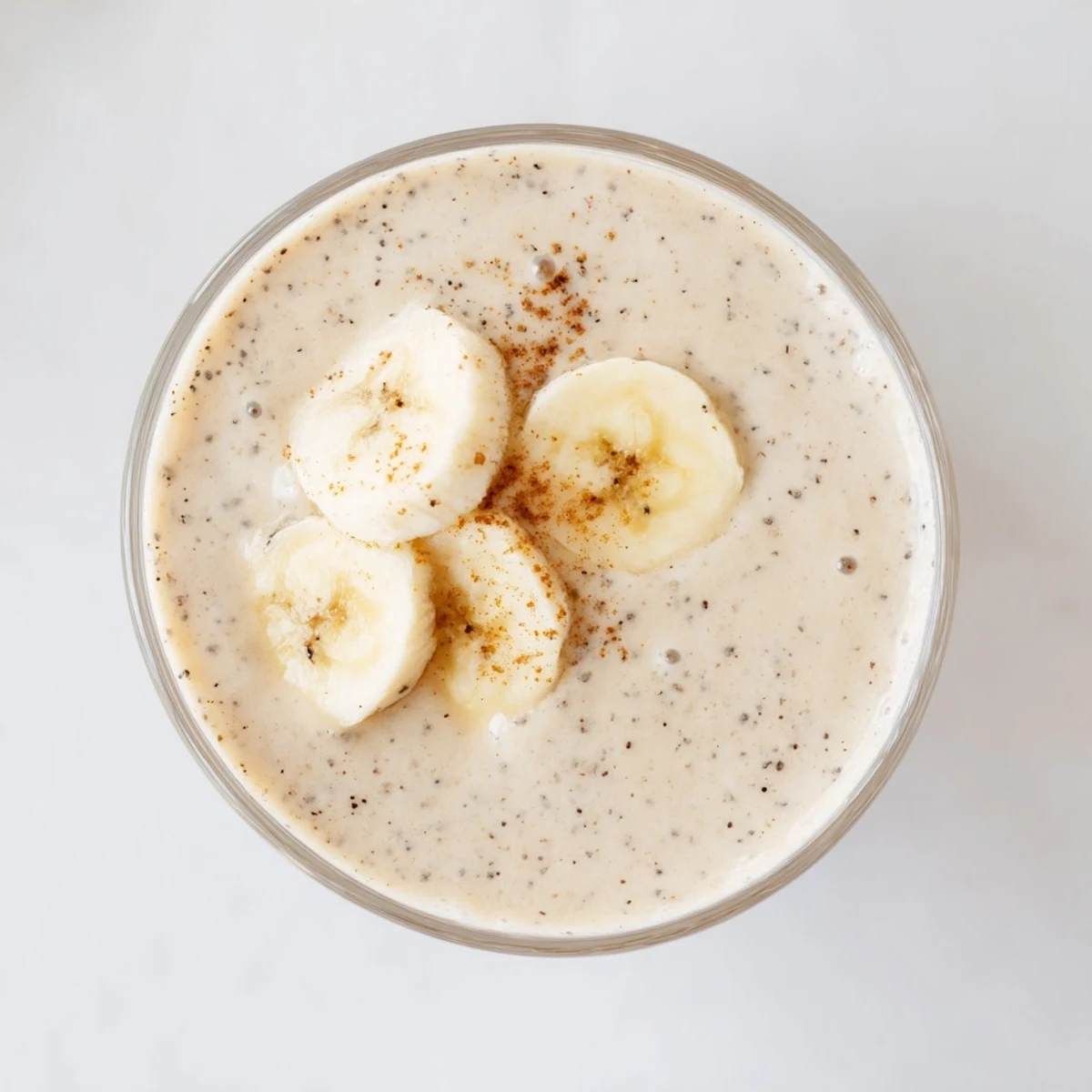 Thick beige Greek yogurt banana smoothie blended with ice and garnished with cinnamon dusting