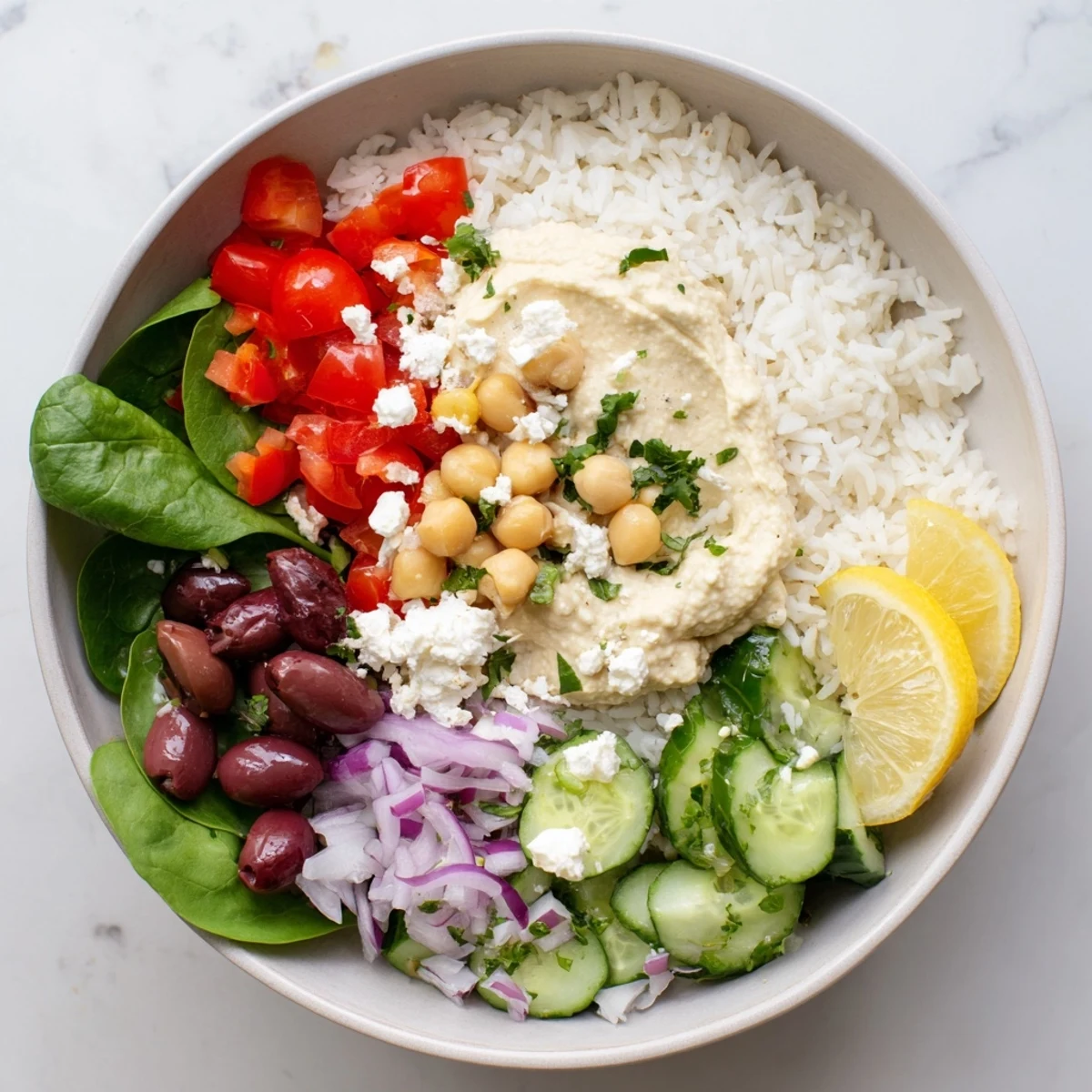 Colorful Mediterranean rice bowl topped with fresh vegetables, hummus, and creamy lemon-tahini dressing