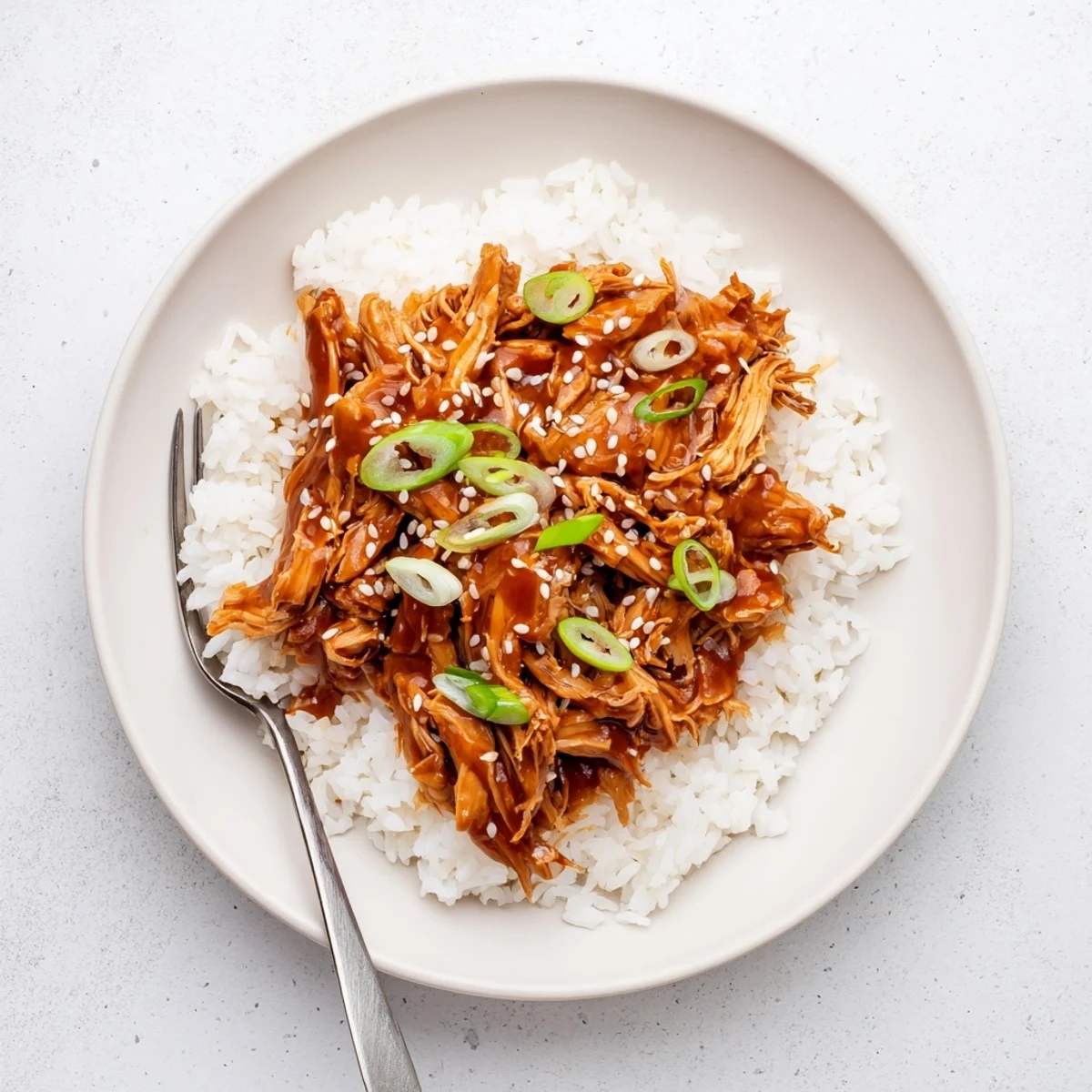 Tender slow cooker Mongolian chicken coated in glossy brown sauce over fluffy white rice