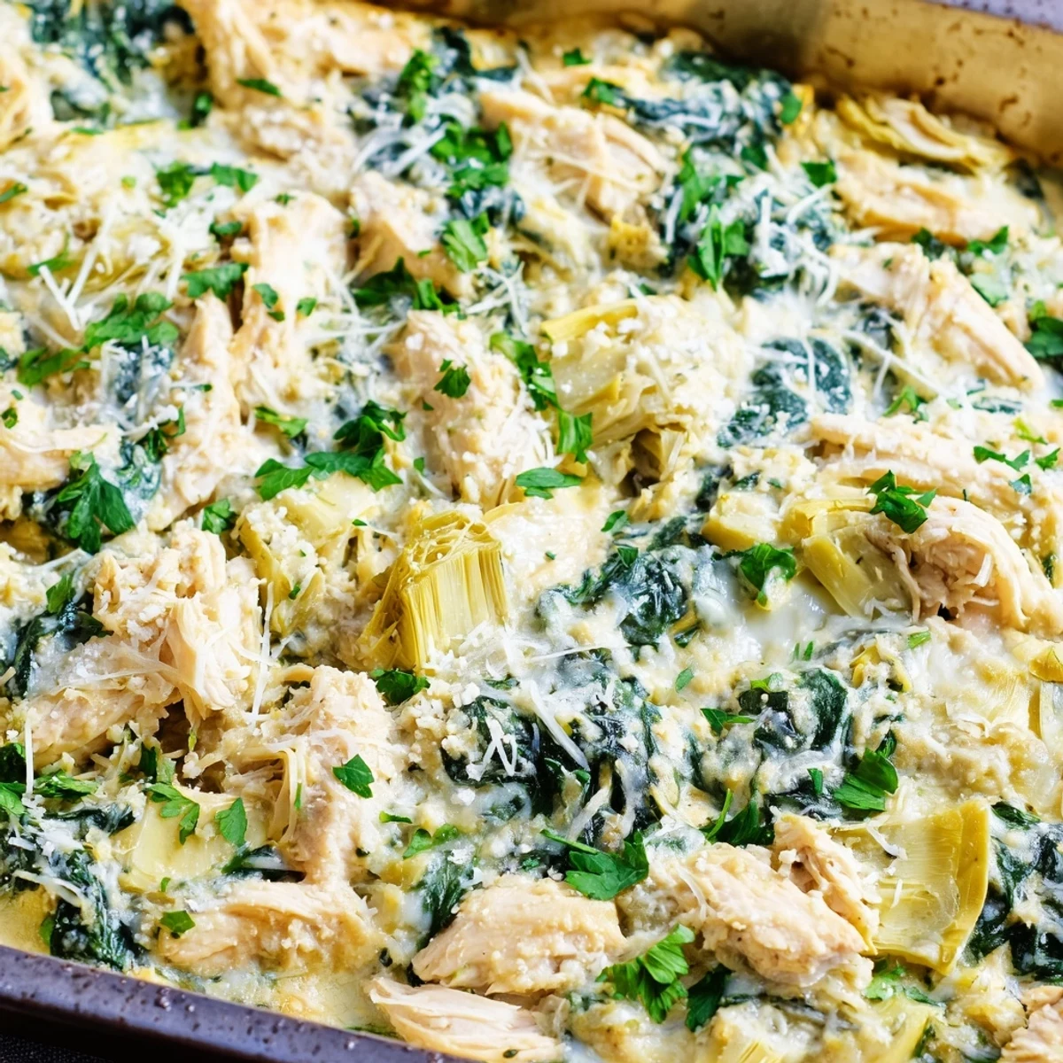 Golden brown spinach artichoke chicken casserole served fresh from the oven with parsley garnish