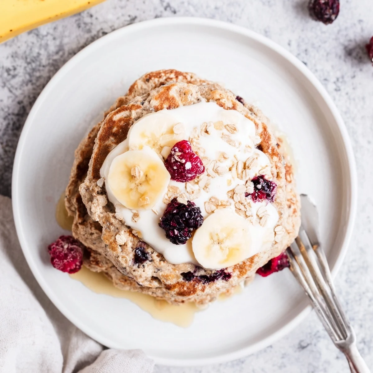Golden stack of fluffy banana oatmeal pancakes topped with creamy Greek yogurt and fresh berries
