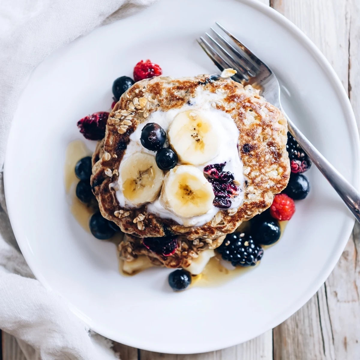 Wholesome banana oatmeal pancakes with Greek yogurt served on a white plate with maple syrup