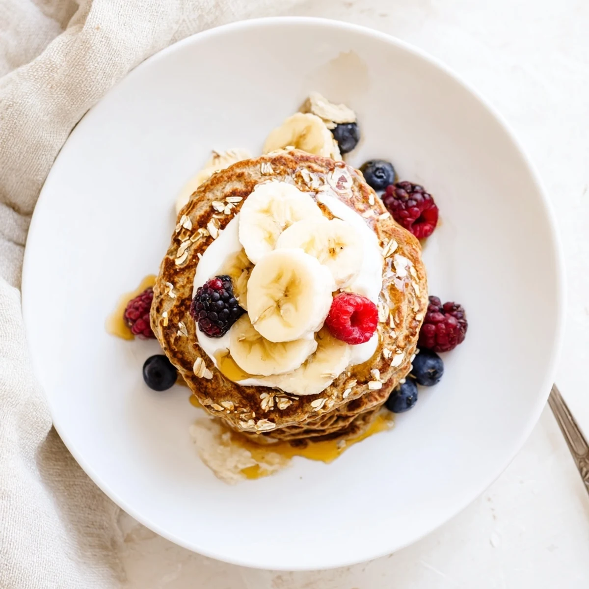 Stack of naturally sweetened banana oatmeal pancakes drizzled with syrup and creamy Greek yogurt topping