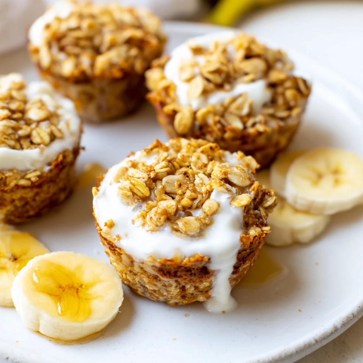 Golden banana baked oatmeal cups topped with a creamy dollop of Greek yogurt and drizzled honey