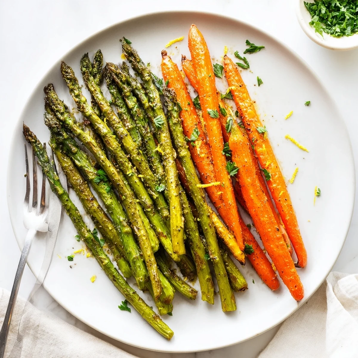 Tender roasted asparagus and sweet carrots drizzled with olive oil and herbs on a parchment lined baking sheet