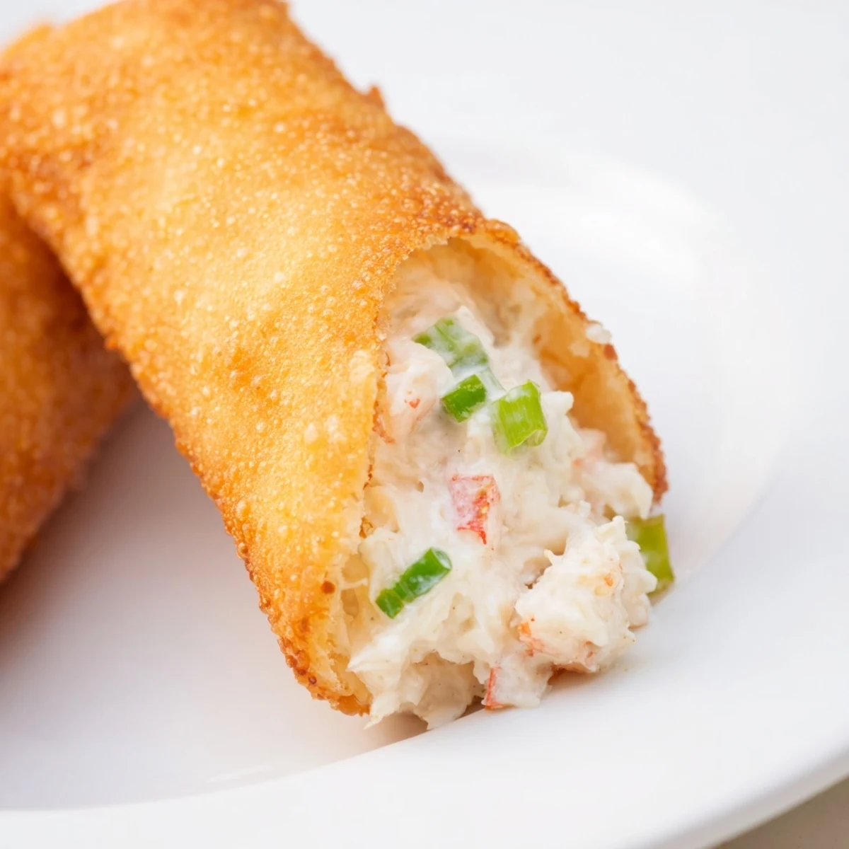 Golden fried Crab Rangoon egg rolls with creamy crab and cream cheese filling plated on white dish