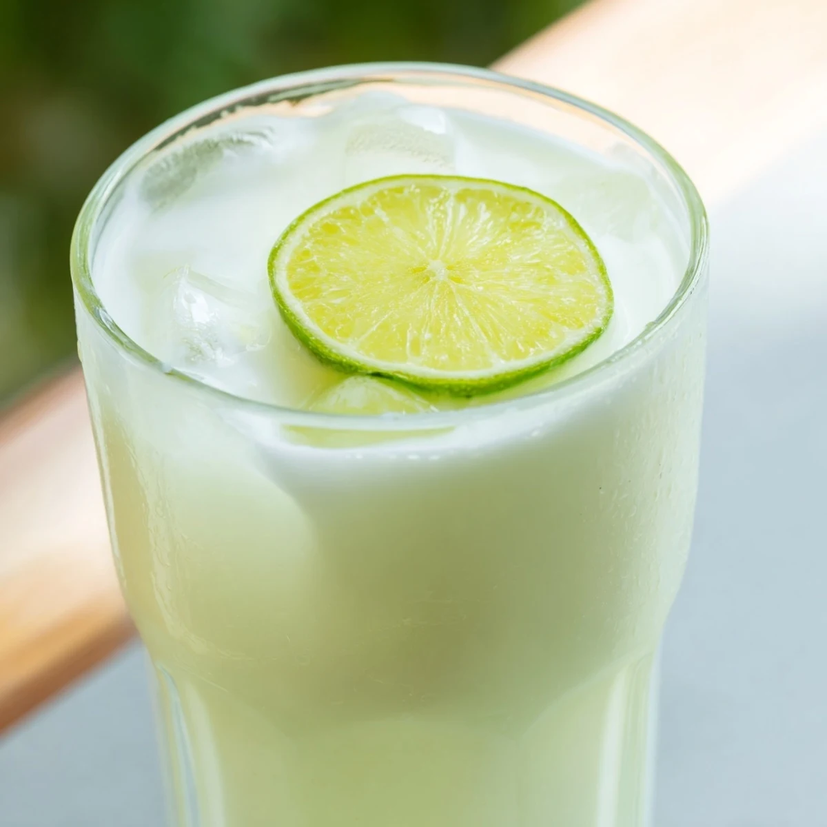 Brazilian lemonade pitcher poured over ice with lime wheel garnish on a wooden table
