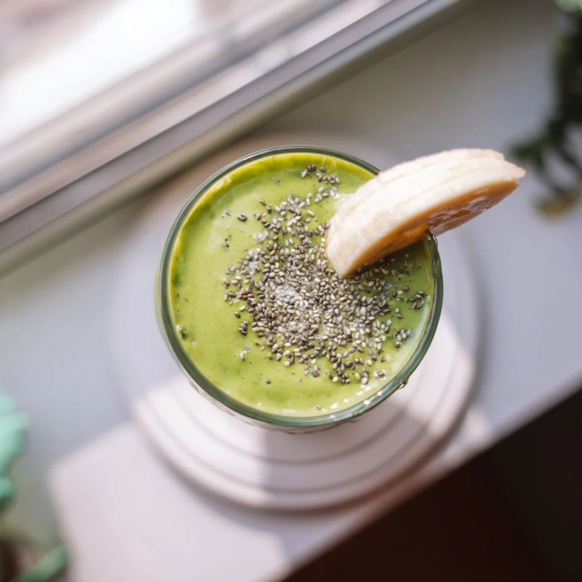 Vibrant green energizing banana matcha smoothie topped with ice cubes in a clear glass on wooden table
