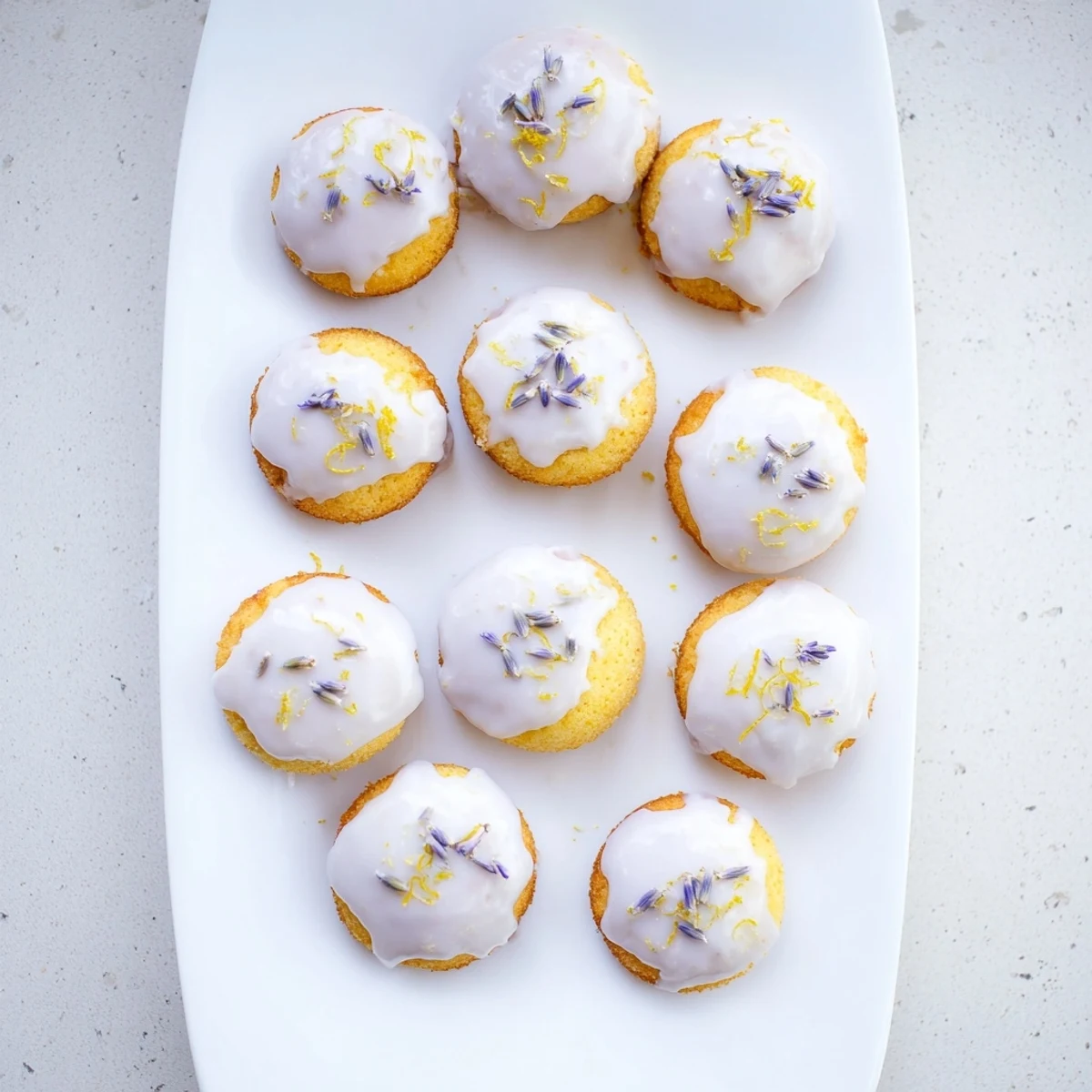 Moist lemon tea cakes topped with pale purple lavender icing and fresh lemon zest garnish