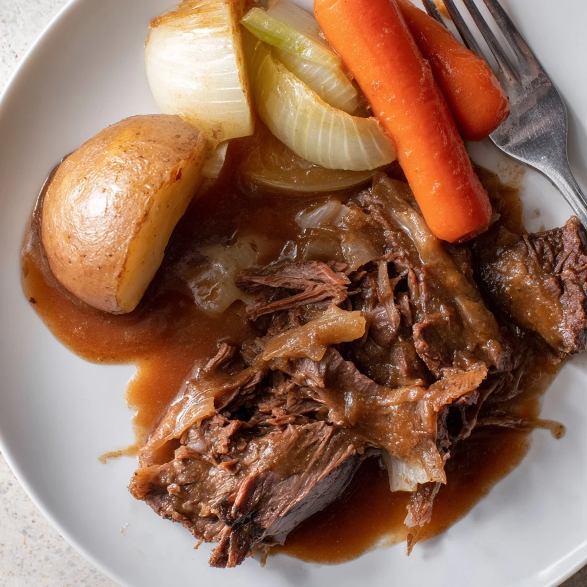 Fork-tender Southern style pot roast plated with roasted vegetables and drizzled with savory beef gravy