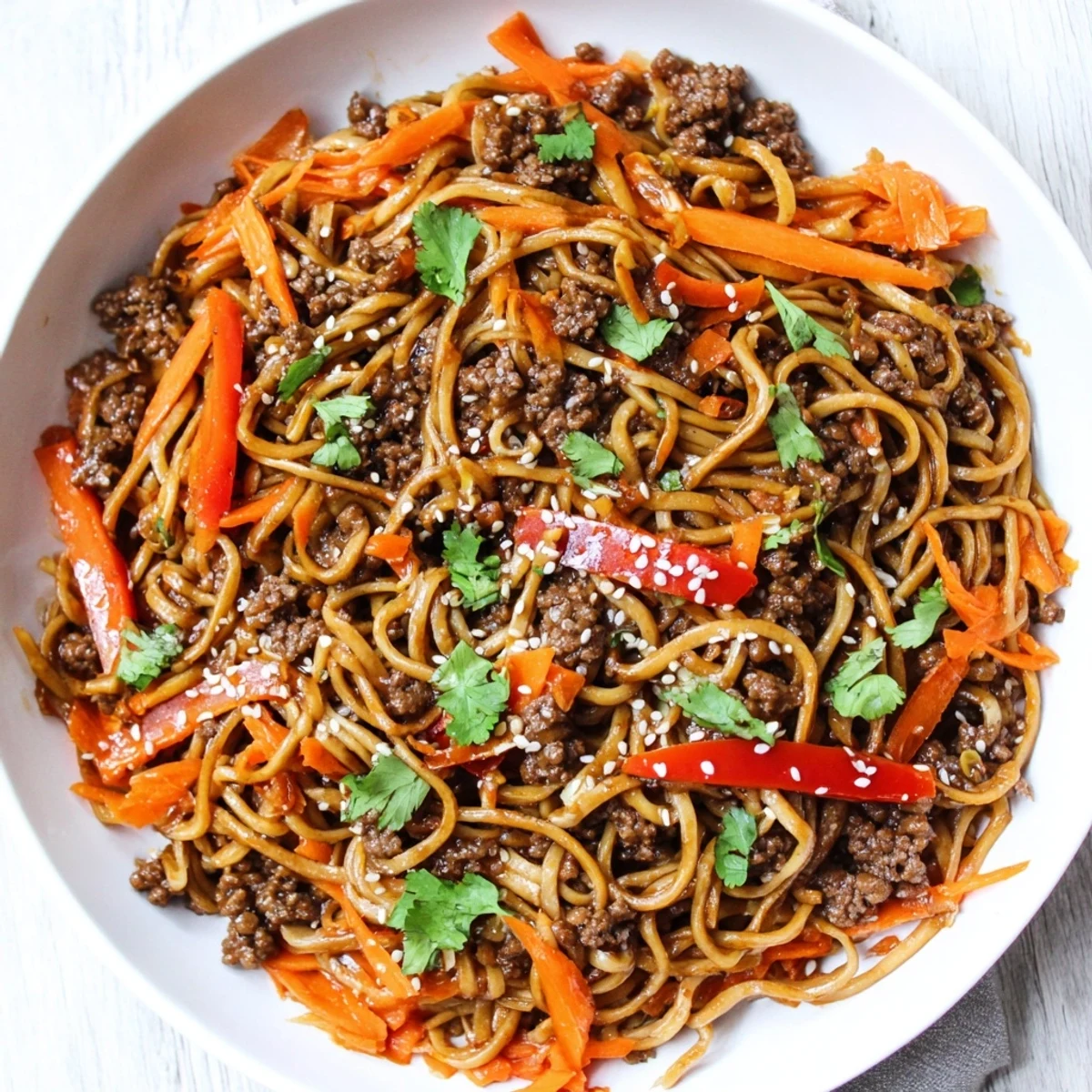 Asian ground beef noodles glistening with savory sauce and colorful vegetables in a wok