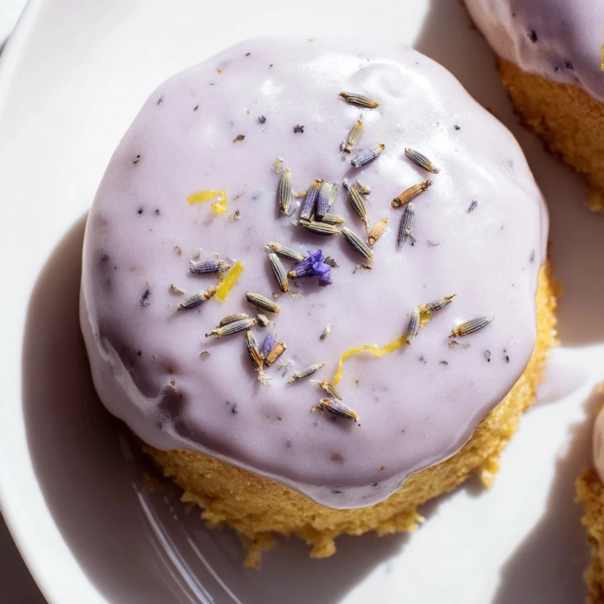 A plate of mini lemon cakes with lavender glaze garnished with citrus zest
