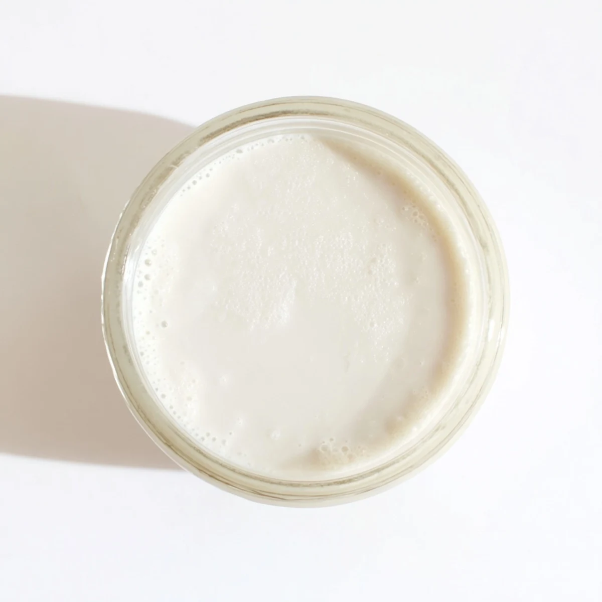 White coconut milk poured into clear glass bottle on wooden counter