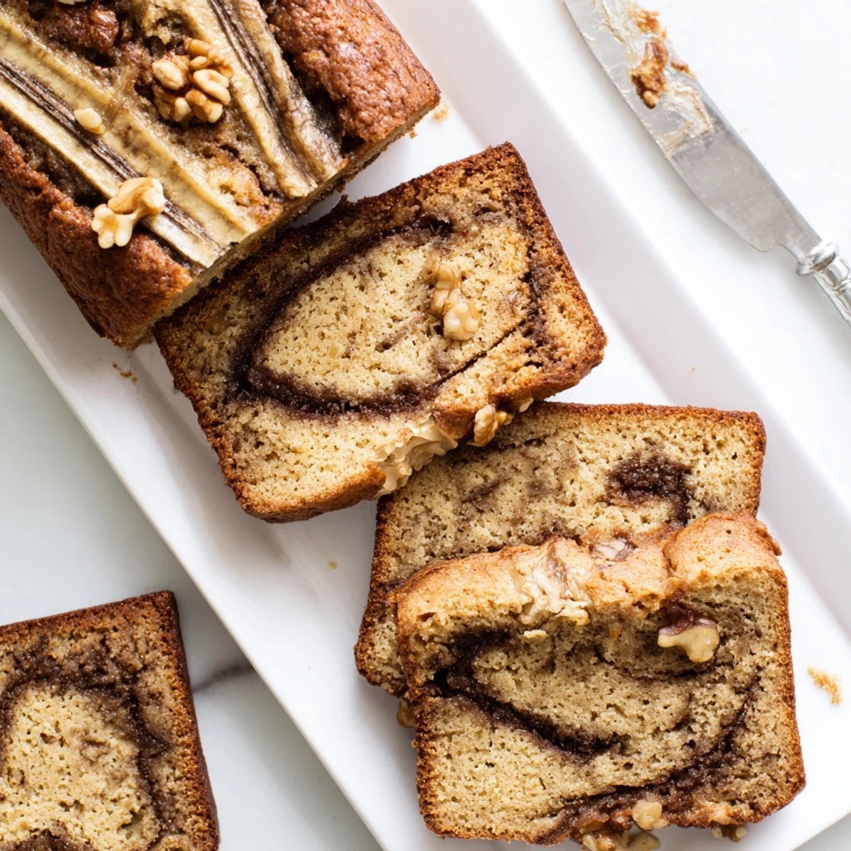 Moist banana bread with walnuts and cinnamon swirl served warm on wooden cutting board