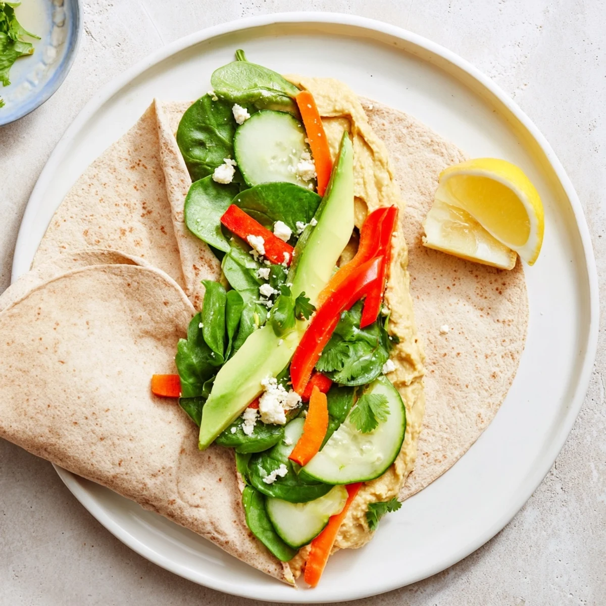 Whole wheat tortillas filled with layered hummus, fresh spinach, and colorful vegetables for a quick Mediterranean lunch
